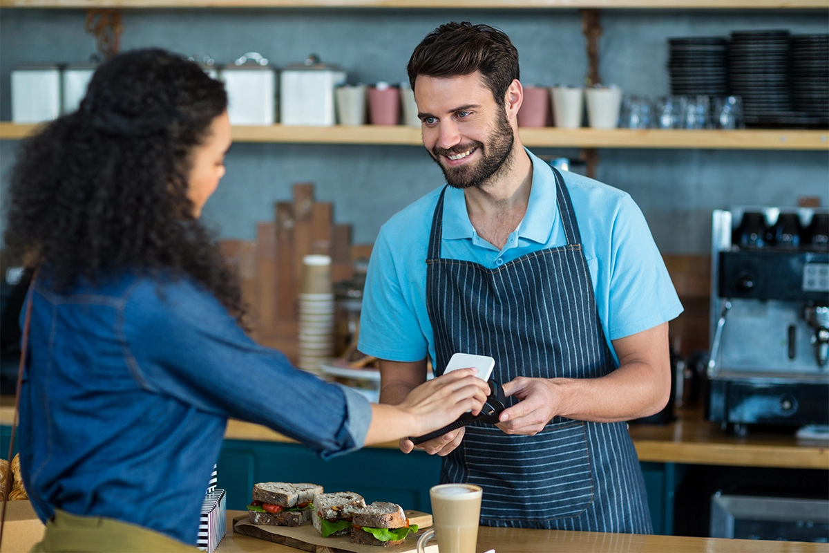 Handsome waiter at the cafe accepts payment from a customer using contactless payment pos machine.